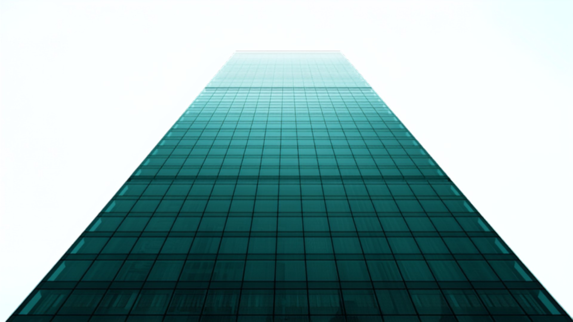 Emerald-tinted glass office tower against a bright sky